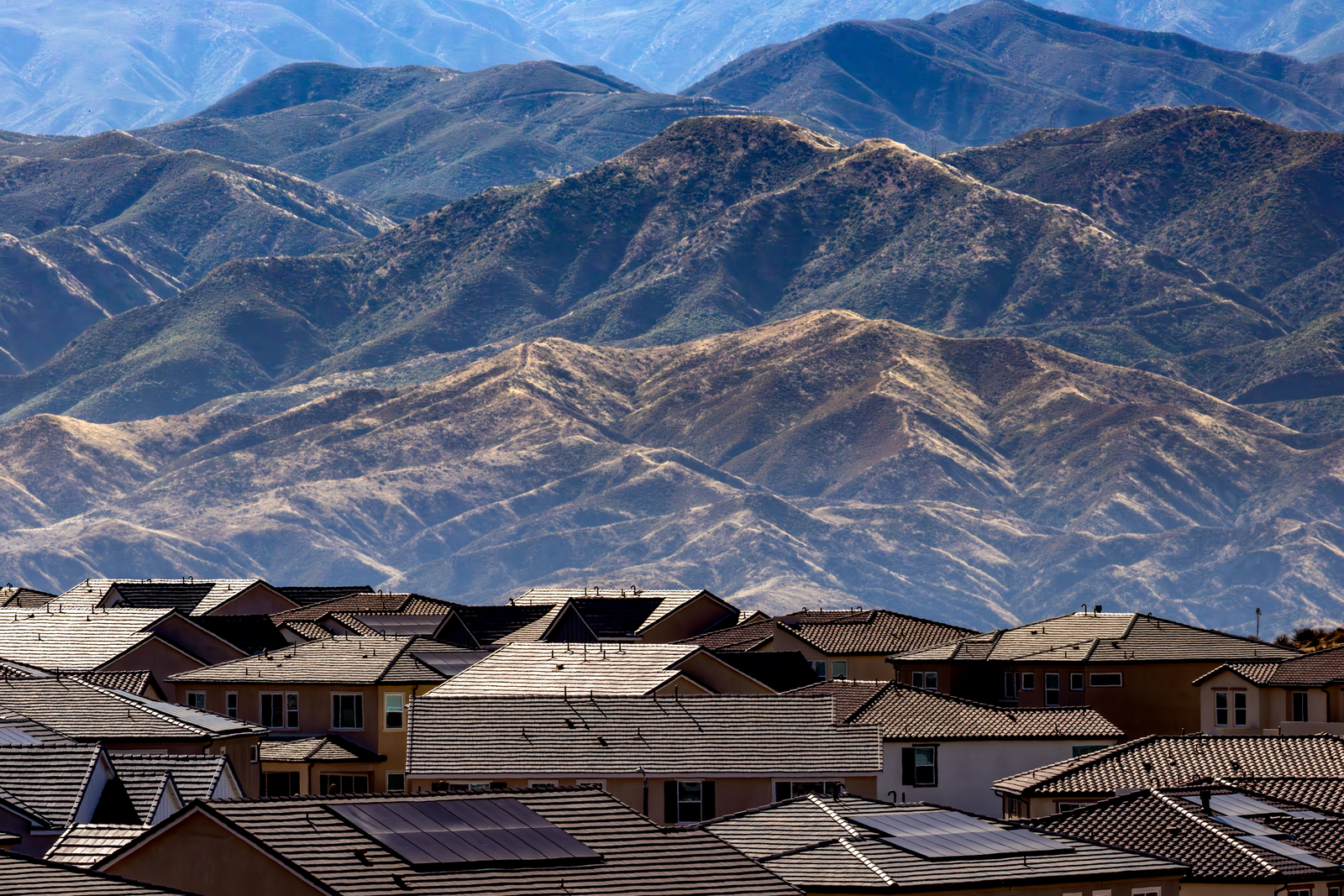 Residential area with houses and solar panels set against scenic mountains.